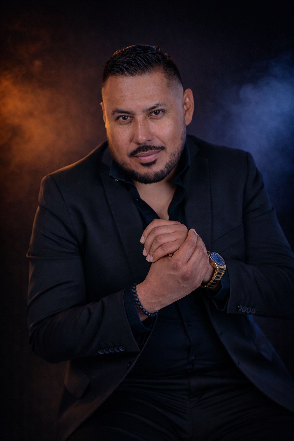 Editorial portrait of a man in a black suit with orange and blue lighting