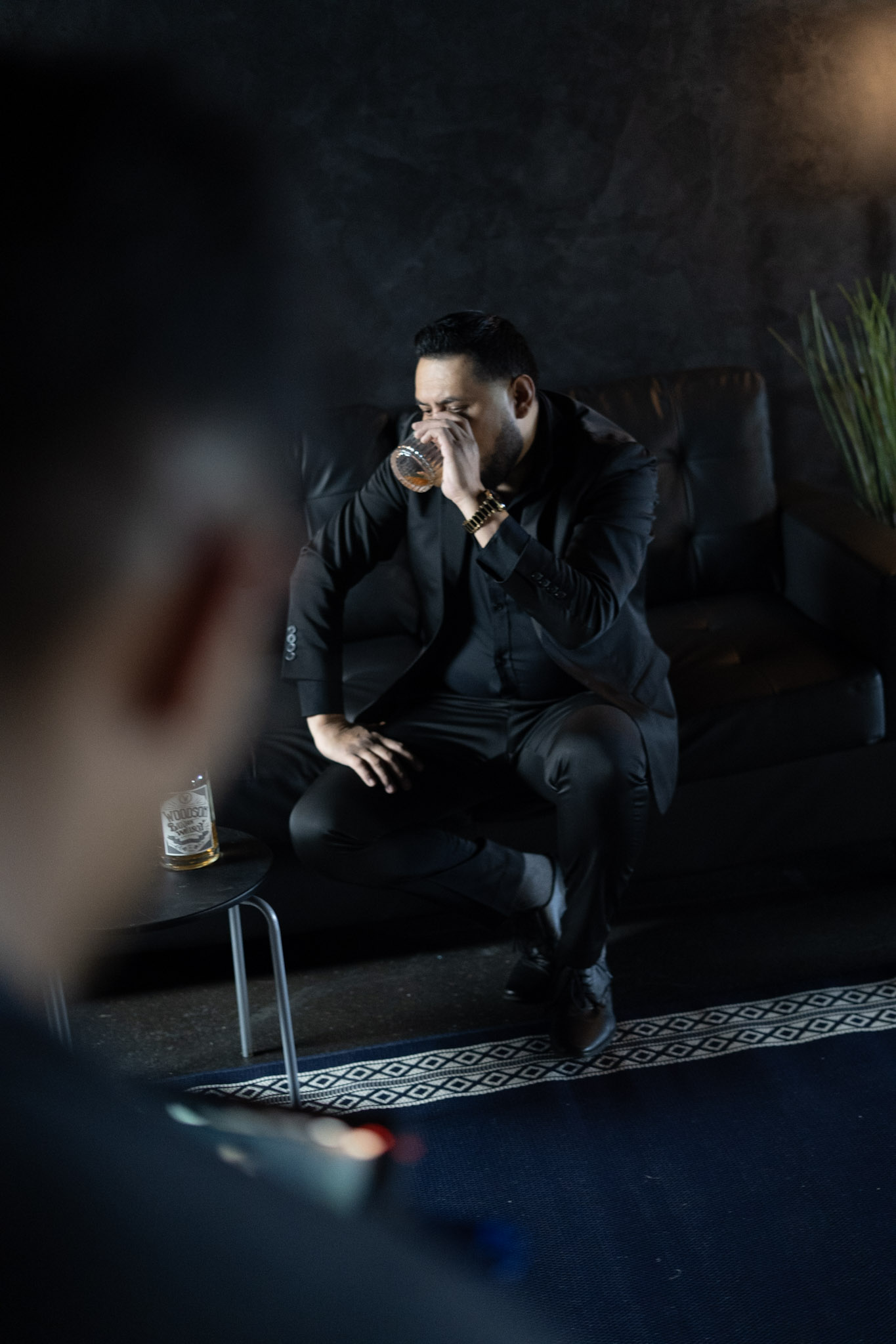 Manuel Quero in a black suit, cinematic low-light portrait on a leather sofa